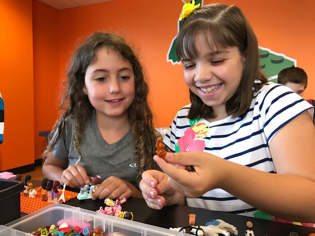Two girls smiling and playing with LEGO bricks