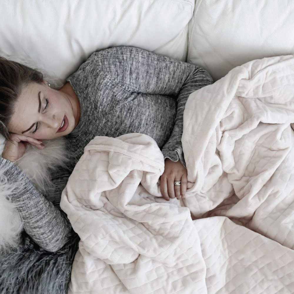Women laying in bed covered in calming weighted blanket