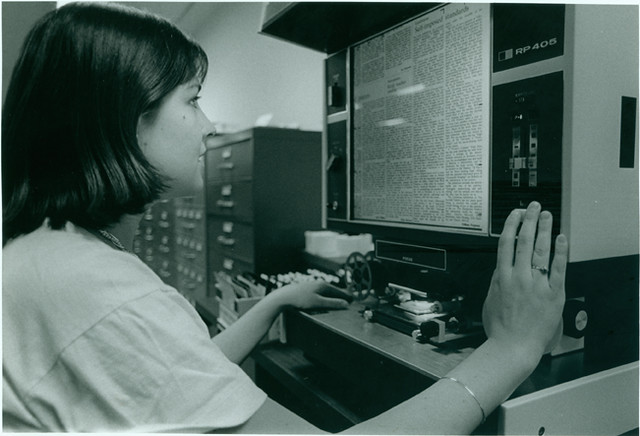 A black and white photo of a student using a microfiche reader