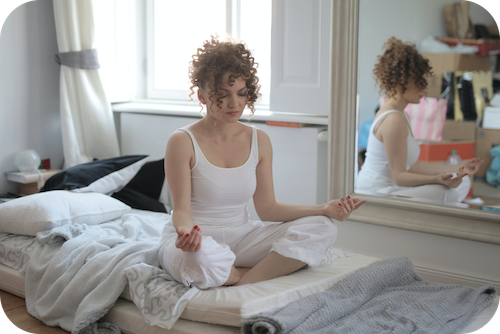 Woman practices meditation in bedroom as stress reduction