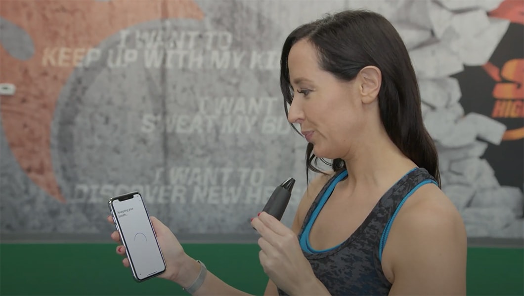 image of woman taking a breath with her lumen metabolism tracker connected to the iphone mobile app at the gym