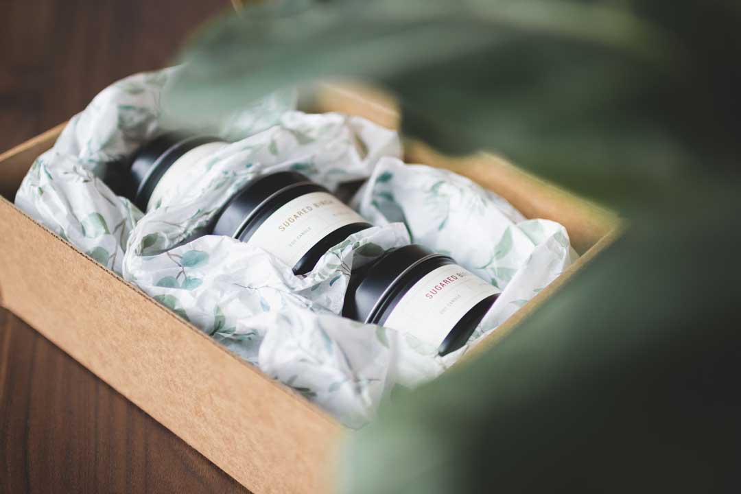 An eCommerce box with small jar candles and tissue paper printed with eucalyptus florals