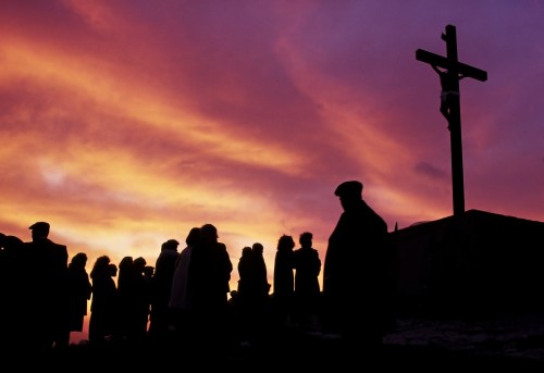 gente al atardecer ante una cruz