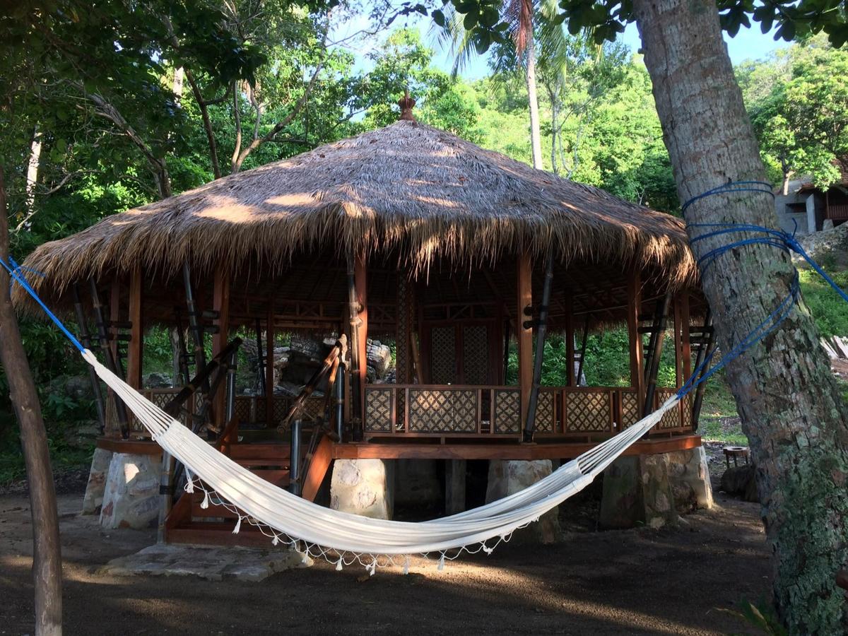 A straw roofed open hut in the forest at Alam Kita, with a hammock strung up between two trees in front