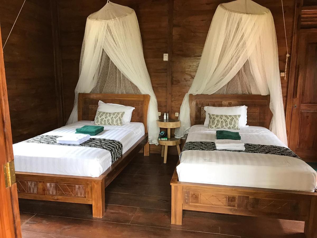 Two single beds at Alam Kita in a wooden panelled room, with mosquito nets above the beds