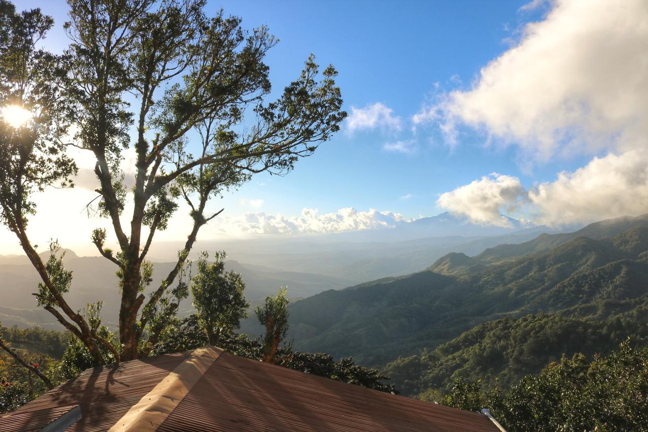 Over the roof of the hostel, the sun is low on the horizon, looking out across a valley in Panama - you can see green mountains and blue peaks in the distance