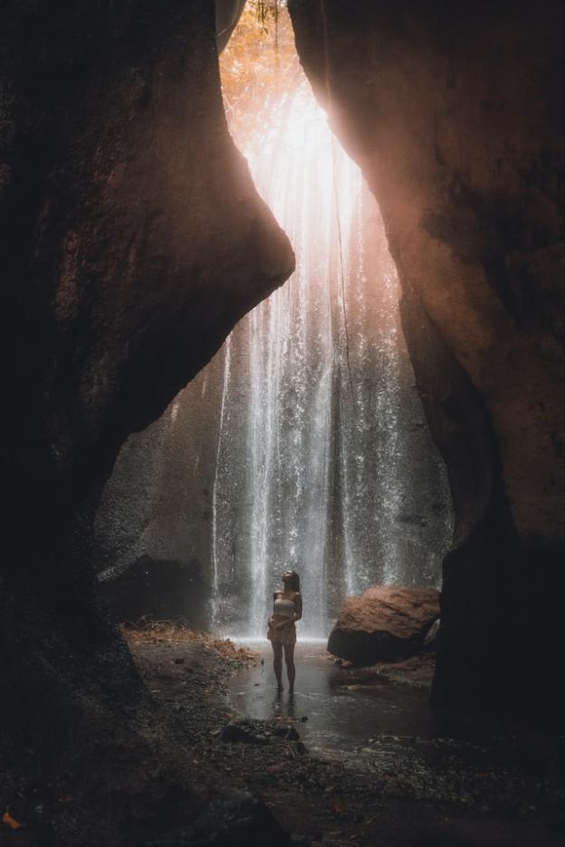 woman standing in a tall cave with a waterfall in the background