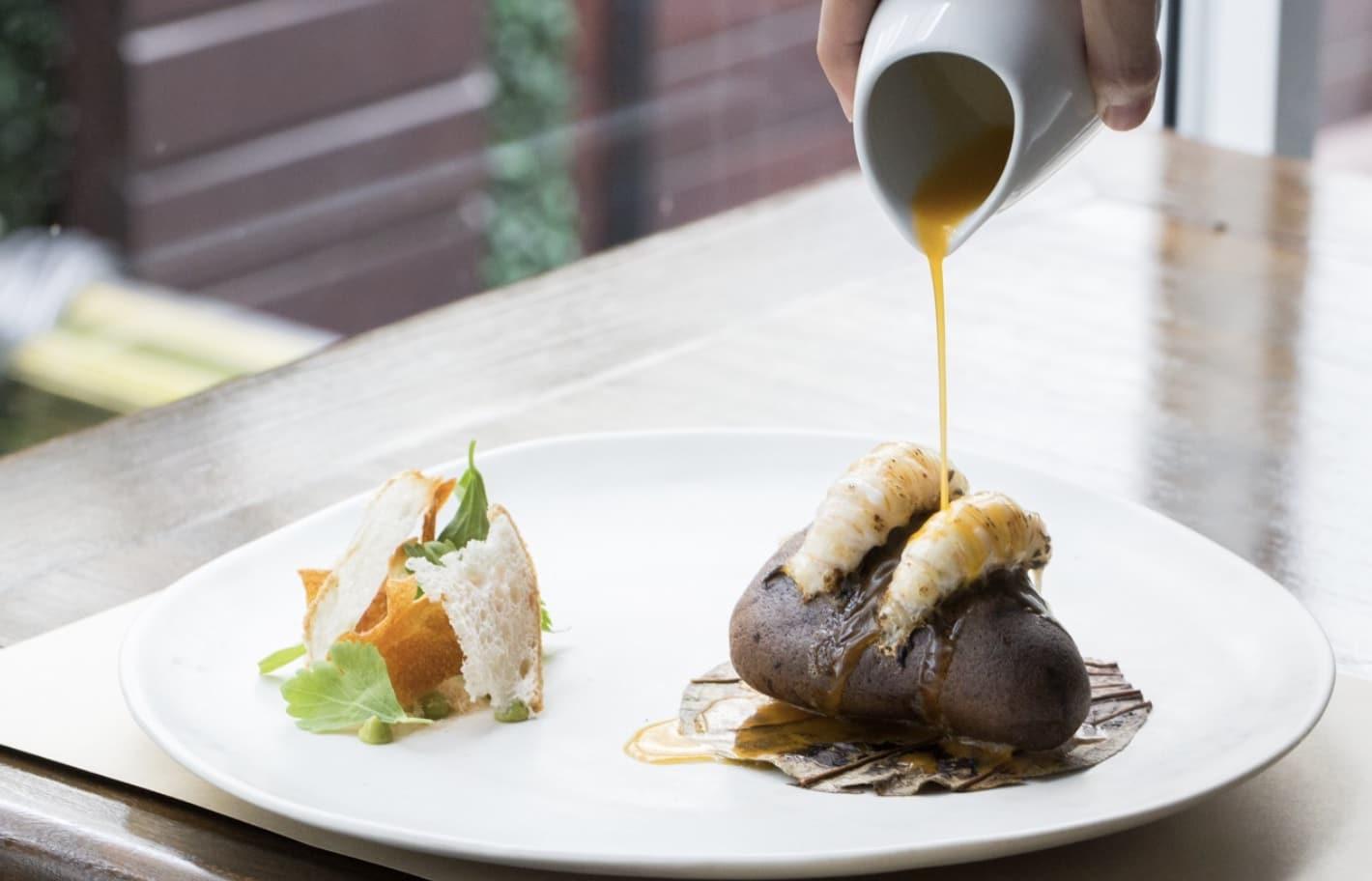 High class dish on table with someone pouring a sauce