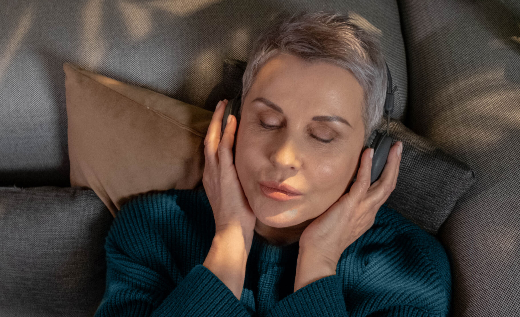 A grinning woman with over-ear headphones on cups her hands over her headphones