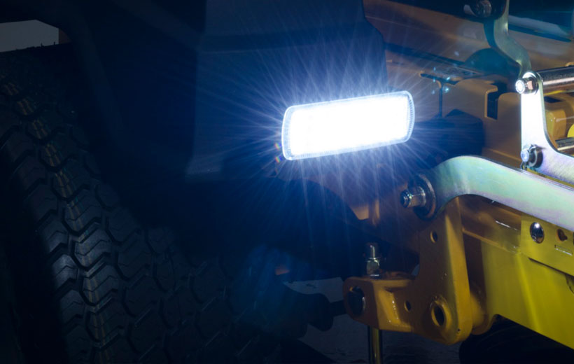 Image of a rectangular light lit up mounted in front of the drive wheel of a mower