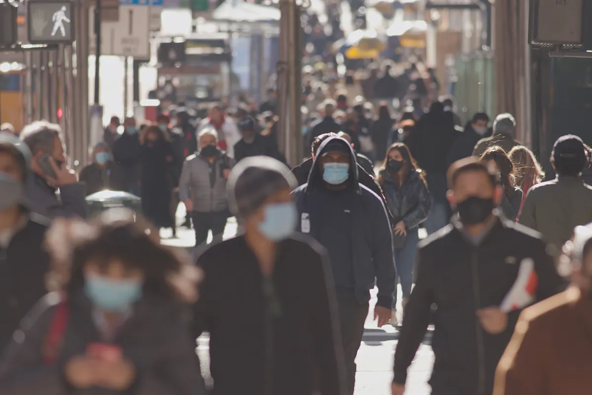 crowds of people walking down a street wearing masks in the uk