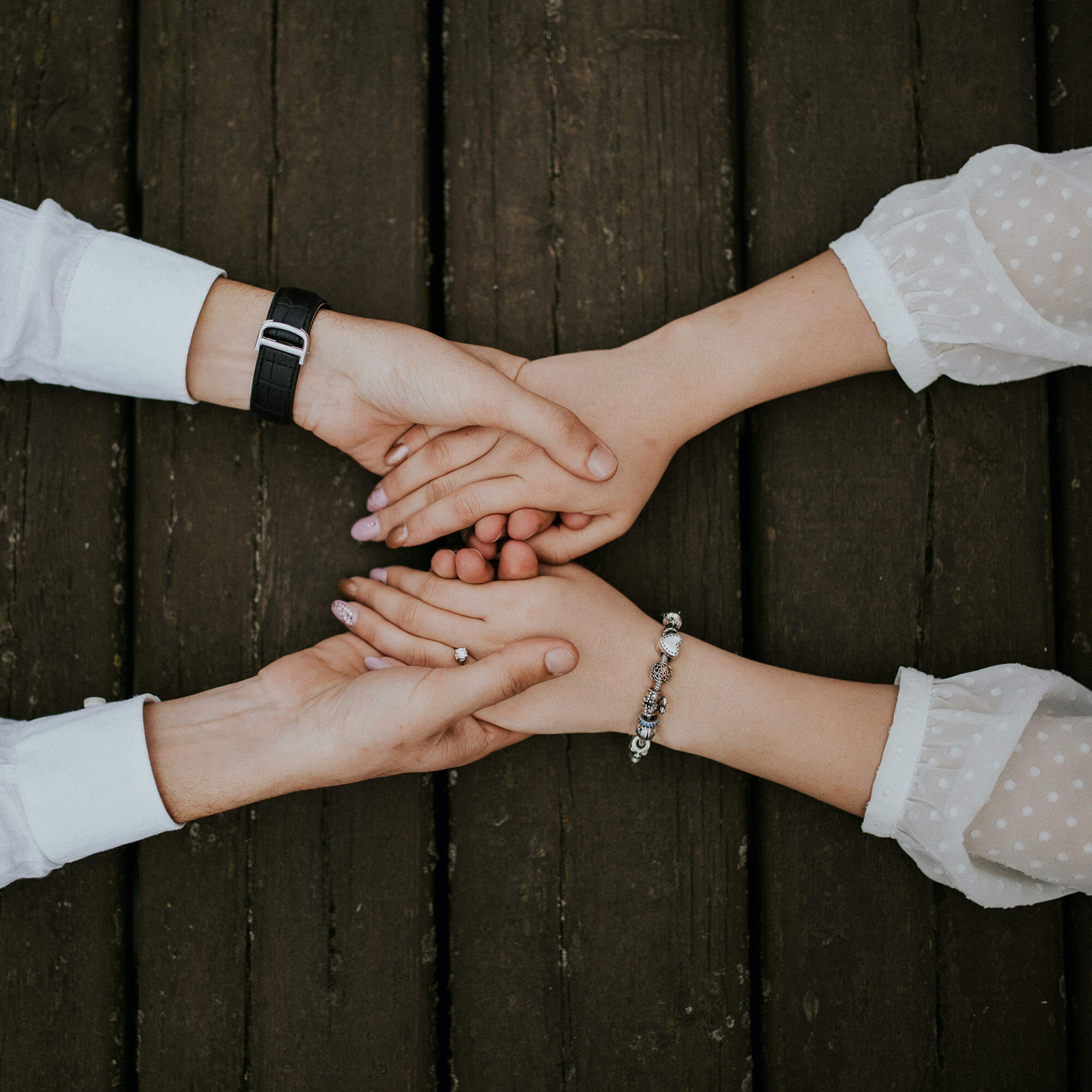 Two pairs of holding hands on top of a wooden table