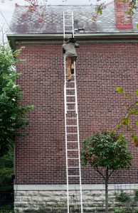 Man climbing ladder to maintain gutters