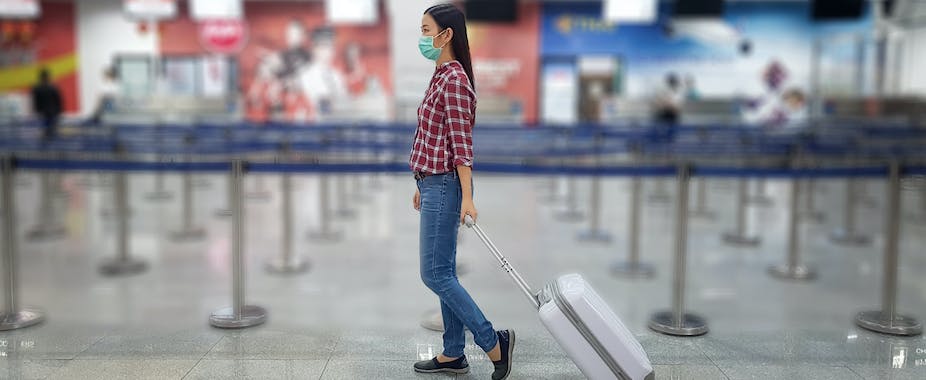 Lone traveler wearing face mask pulling suitcase in empty airport queue