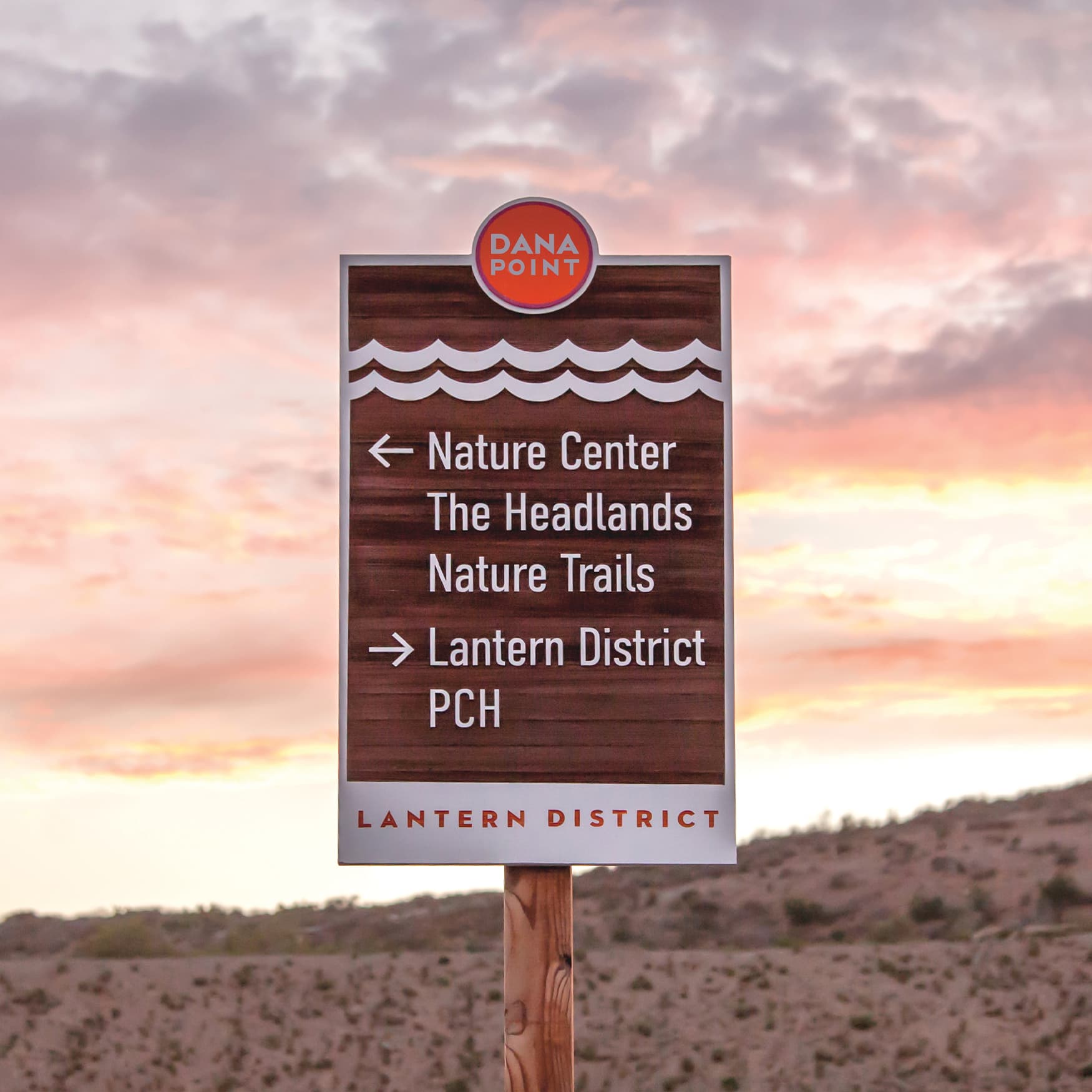 City of Dana Point wood wayfinding sign with hills and sunset in the background