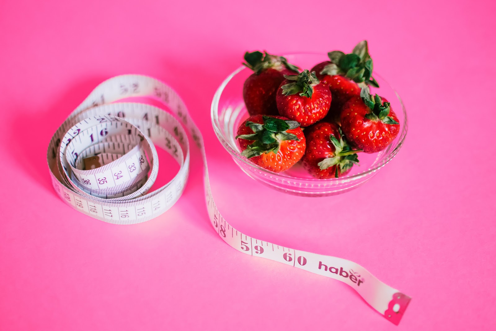 A waist measuring tap next to a bowl of strawberries