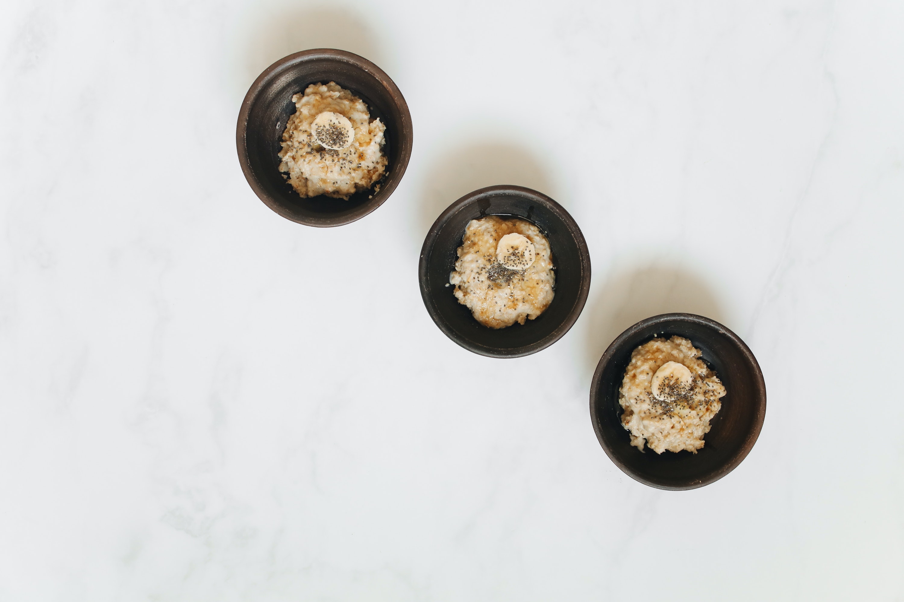 Three bowls of oatmeal with toppings lay diagonally across a white background.