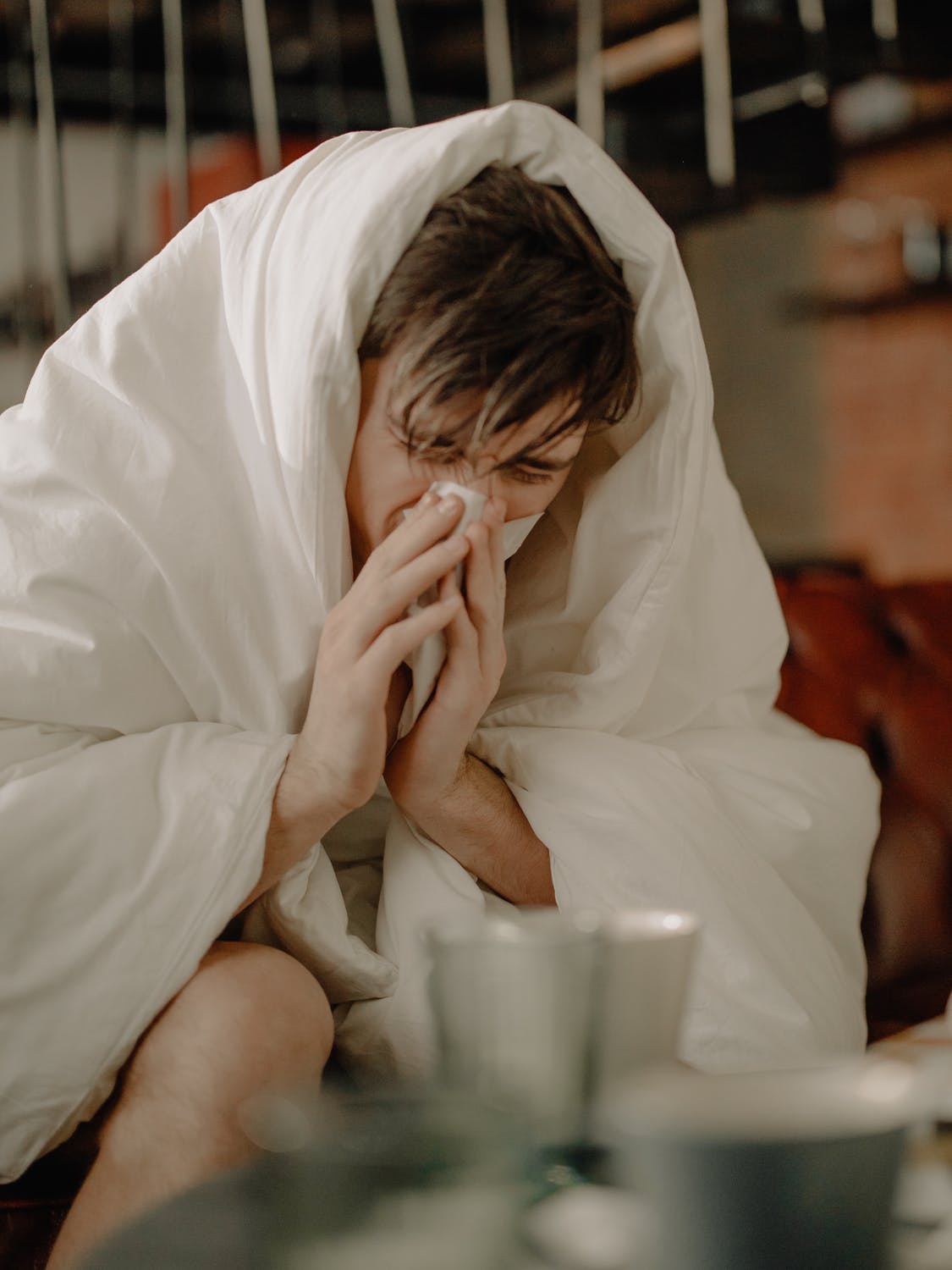 Wrapped in a blanket, a sick teenage boy blows his nose.