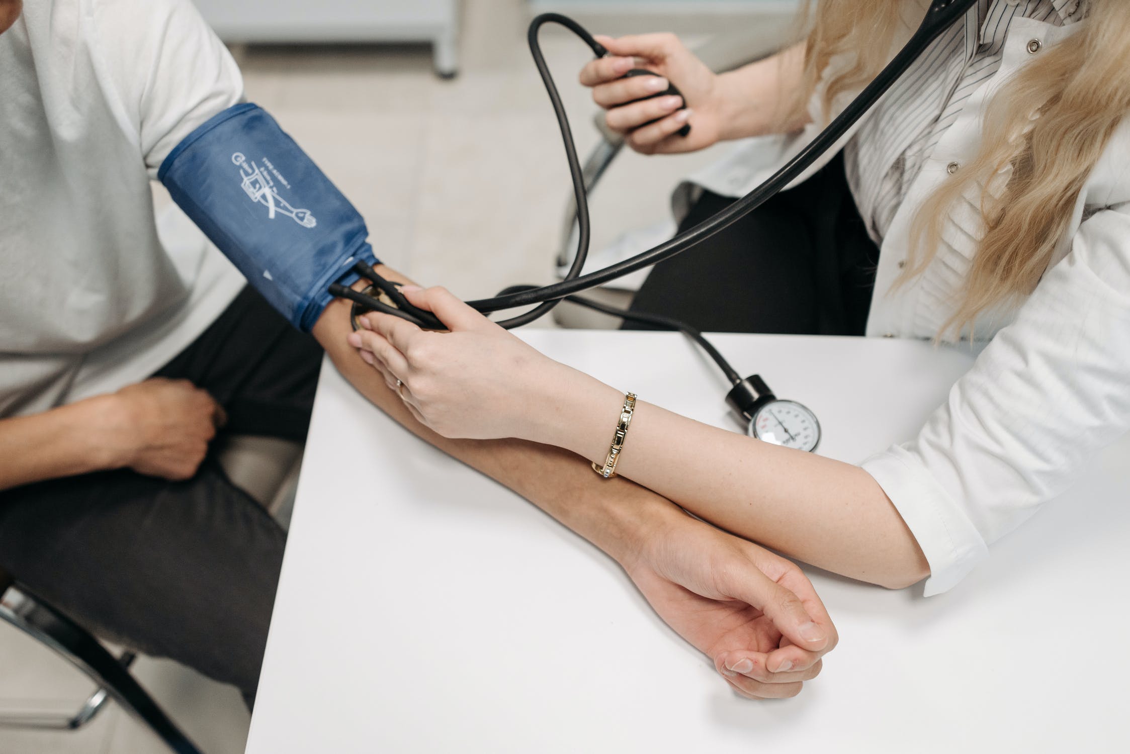 A female doctor takes a male patient's blood pressure over a table.
