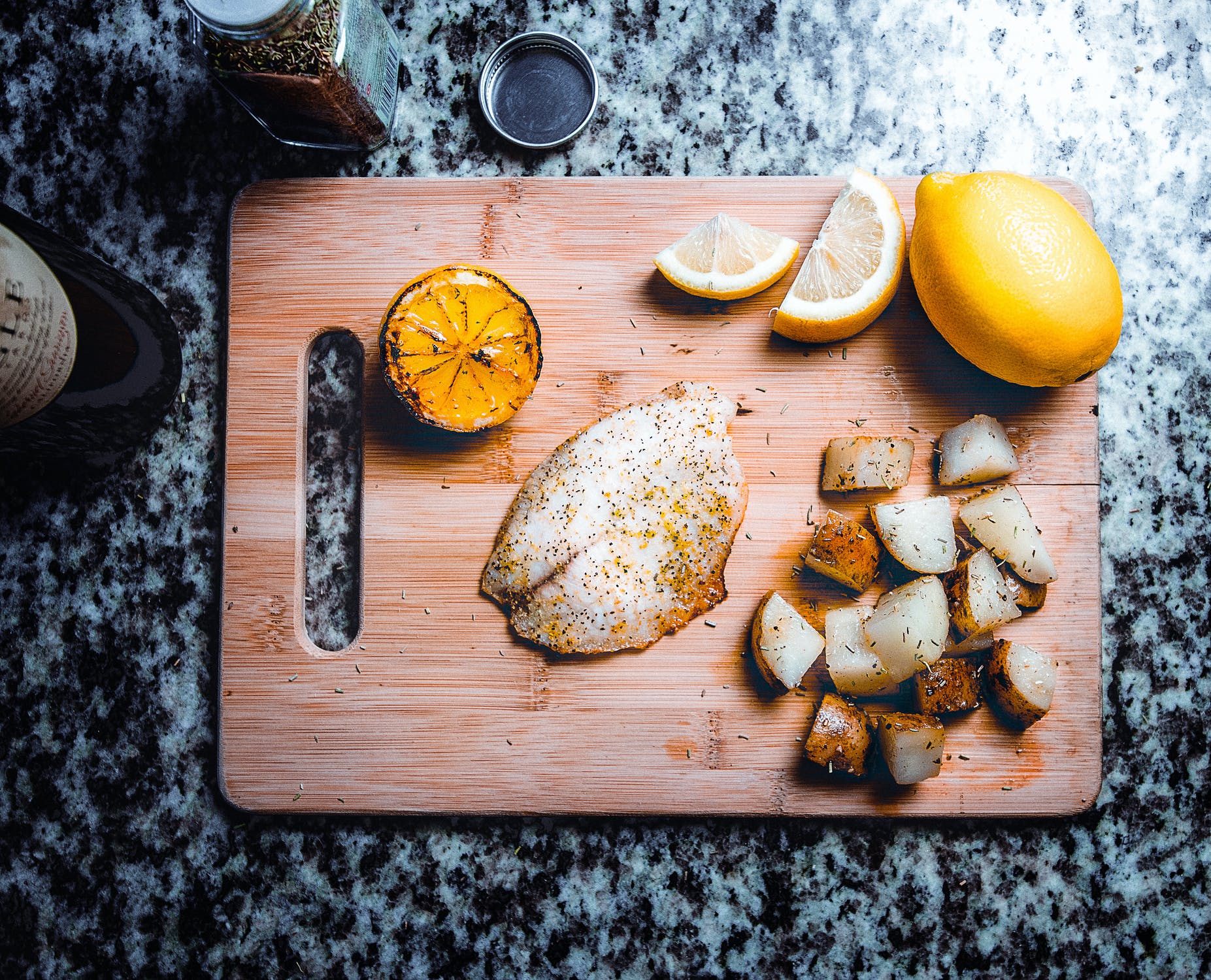 Seasoned fish on a cutting board with lemon and potatoes.