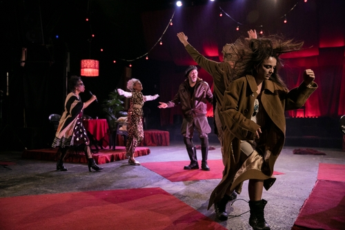 Performers dancing on stage, there are red lights hanging from the ceiling and red rugs on the floor