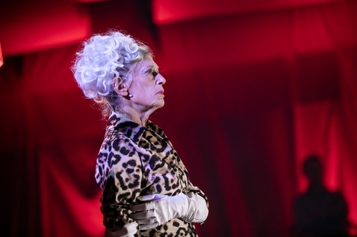 Onni Johnson (Clytemnestra), an older white woman, on stage wearing gloves and an animal print dress