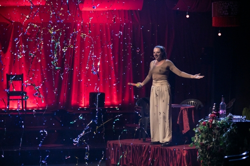 Mattie Barber-Bockelman (Electra), a young white woman, on stage holding a confetti cannon with sparkly confetti in the air