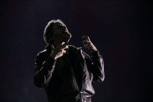 George Drance (Agamemnon), an older white man, alone dimly lit in a white light