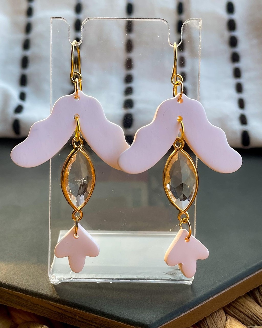 Dangly polymer clay earrings in white, two wavy and arrow-like pieces held together by a marquise-shaped clear gem, the bottom shape much smaller than the top.