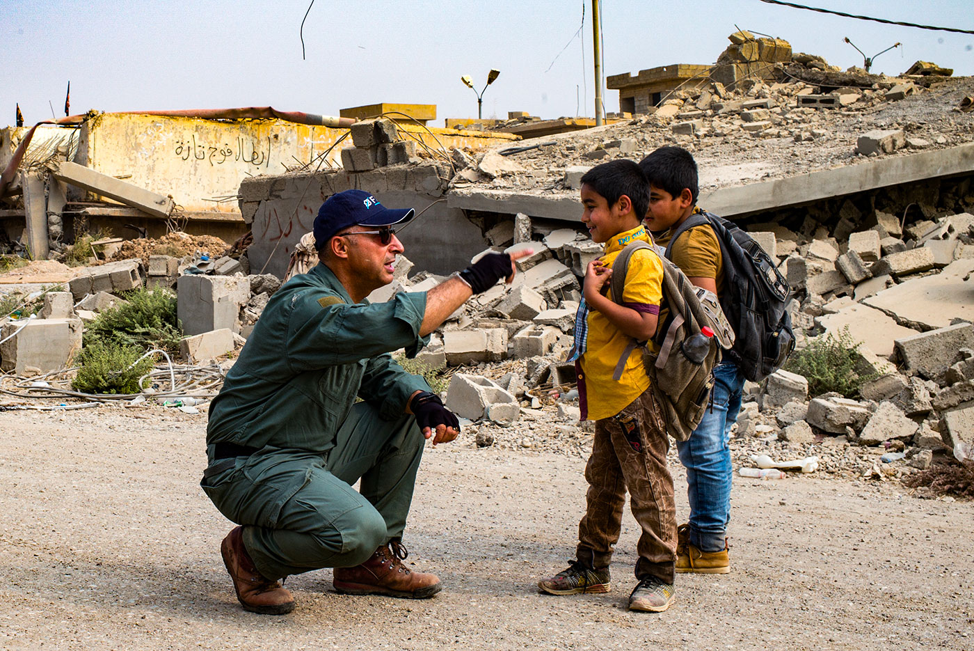 A squatting man talking to 2 boys