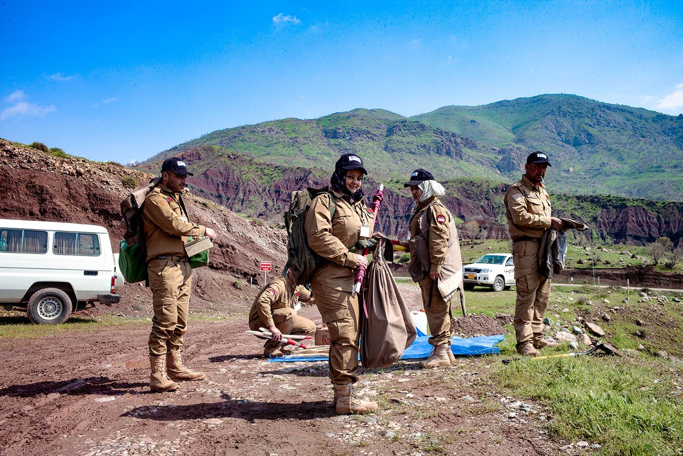 5 deminers in the field and the women in the center similing