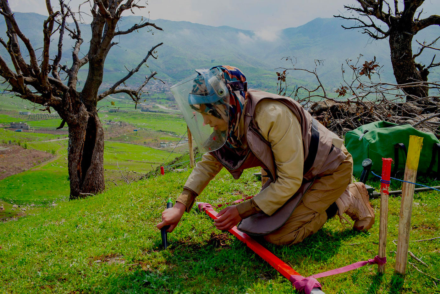 A female deminer kneeling on the ground and demining