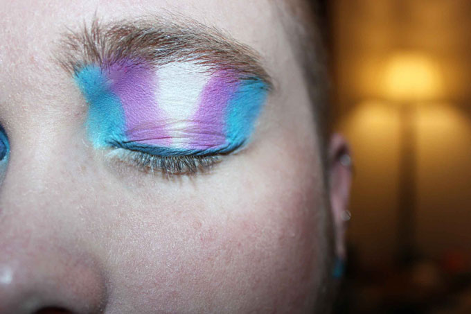 A closeup view of a blue, purple, and white trans flag painted on an eyelid