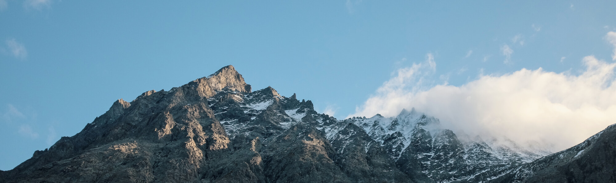 A snow-covered mountain, a cloud, and blue skies.