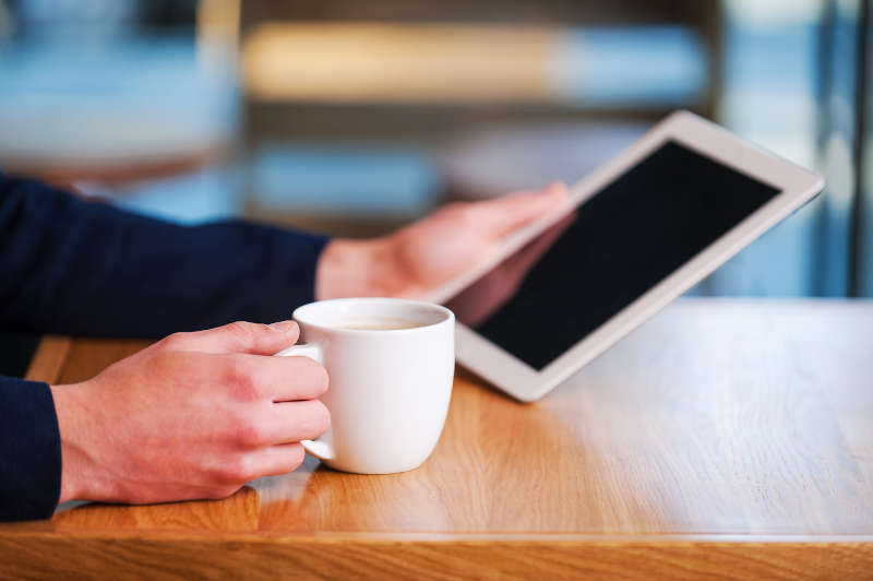 Kopje koffie drinken met een tablet in de hand