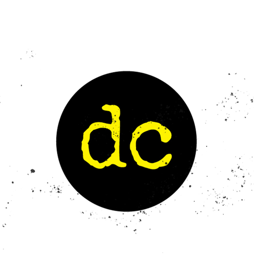 A black circle logo with dc in yellow typewriter font. The logo is distressed with ink splatter on and around it.