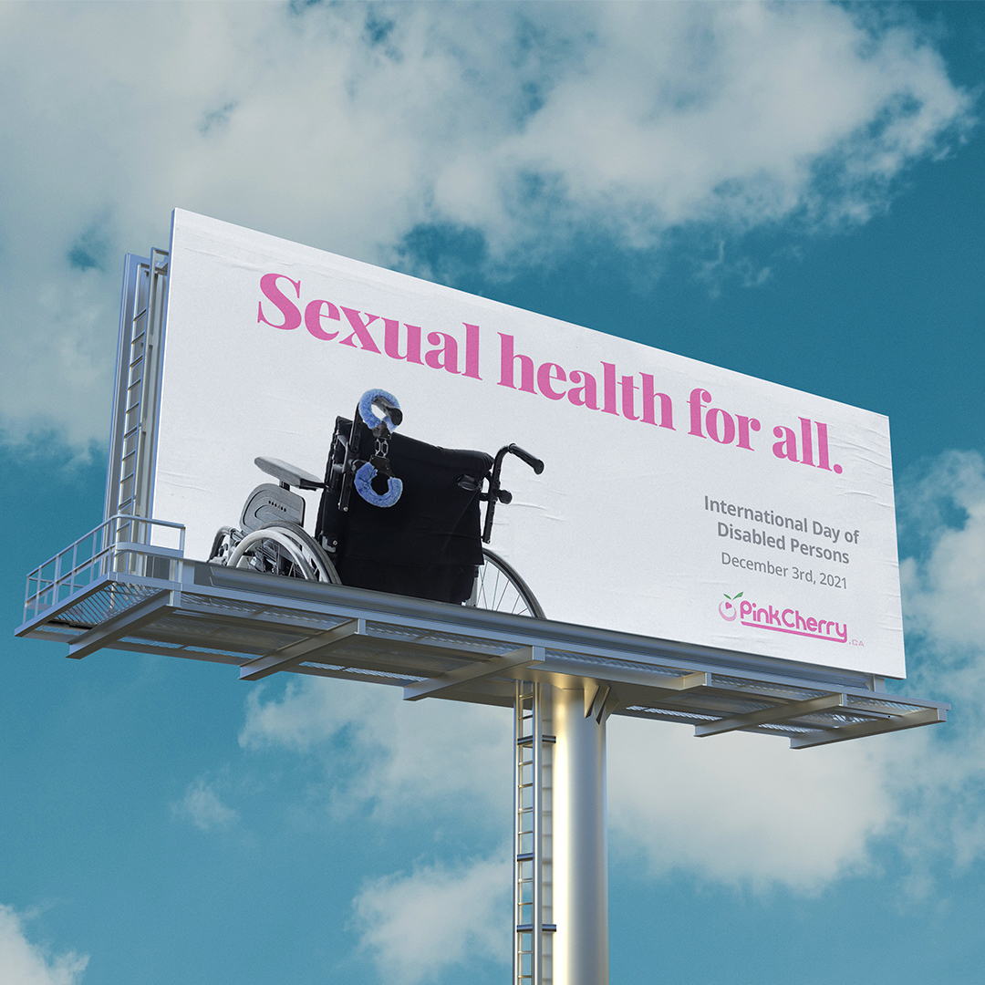 A billboard agains a blue sky. The all white background with large pinnk type that reads "Sexual health for all." A wheelchair is cropped off the bottom left of the billboard with type on the right that reads "Internatioanal Day of Disabled Persons" and the Pink Cherry logo at bottom of billboard.