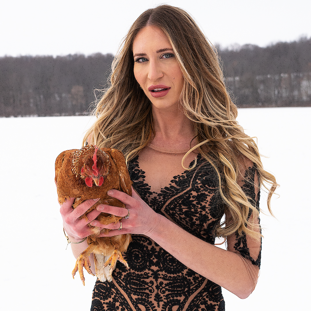 Photograph a a figure with long blonde hair and lace dress holding a chicken in a snowy field.