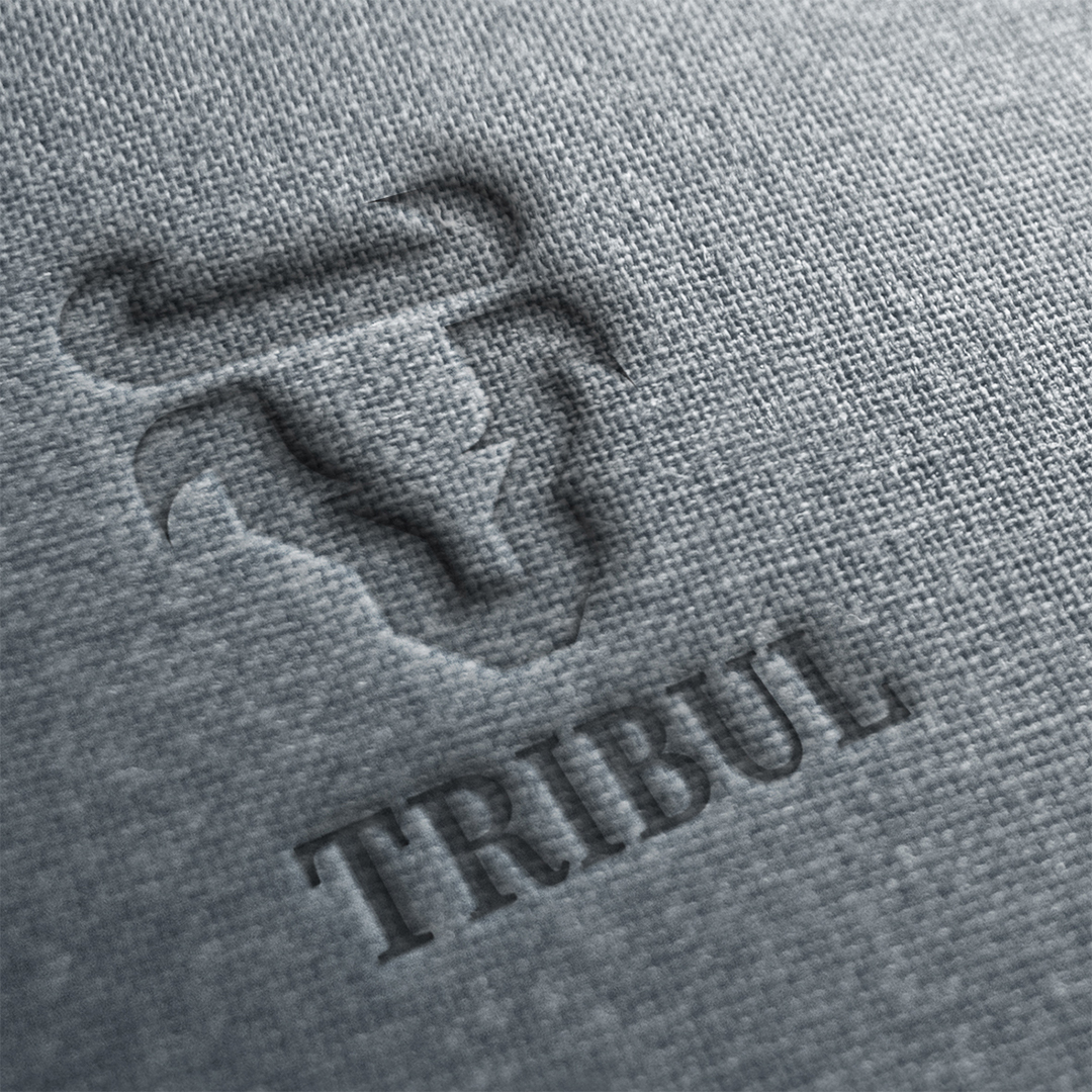A logo for a company called Tribul with a stylized bullhead with horns imprinted on a rough grey fabric surface.