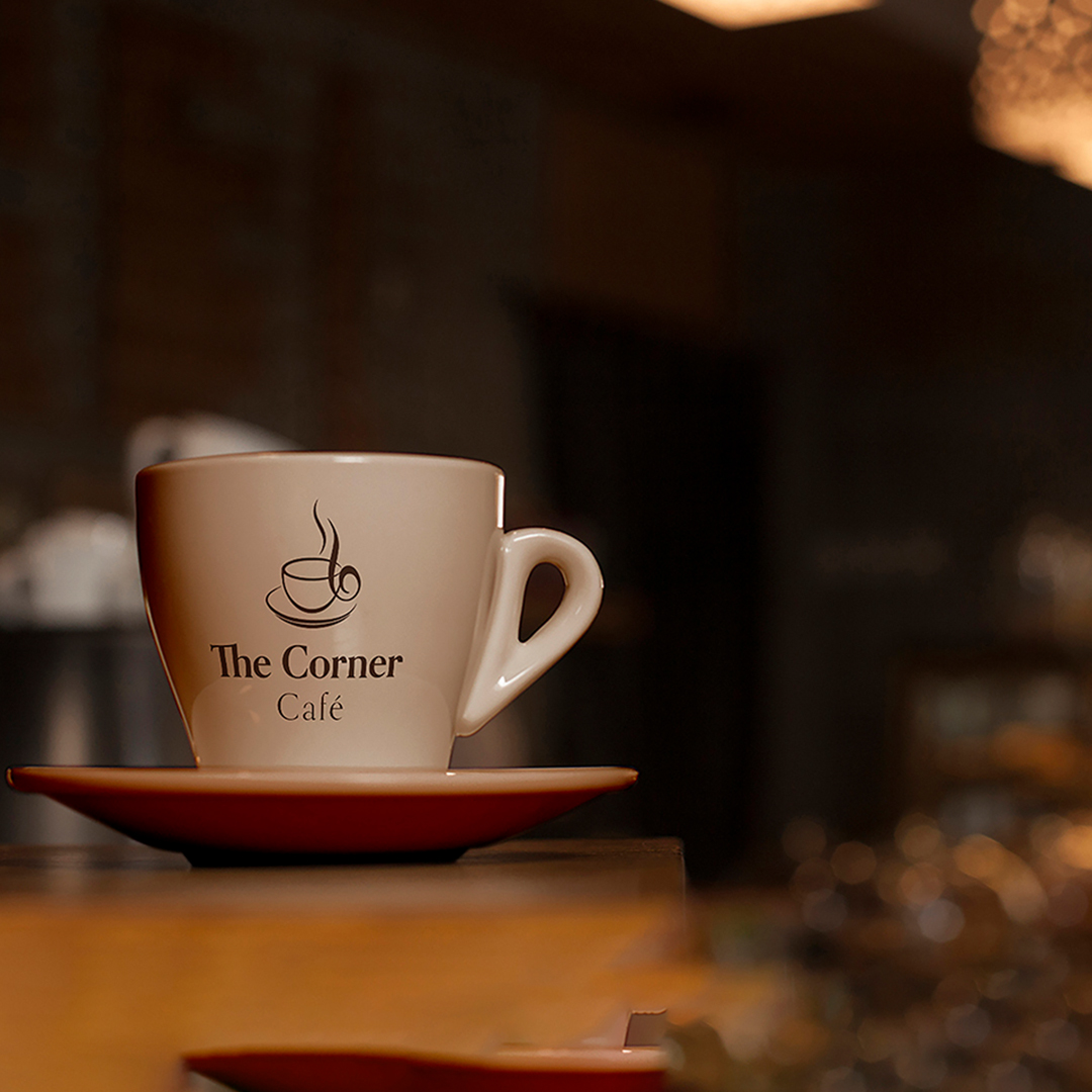 A coffee cup with the logo "The Corner Café" sits on a wood table.