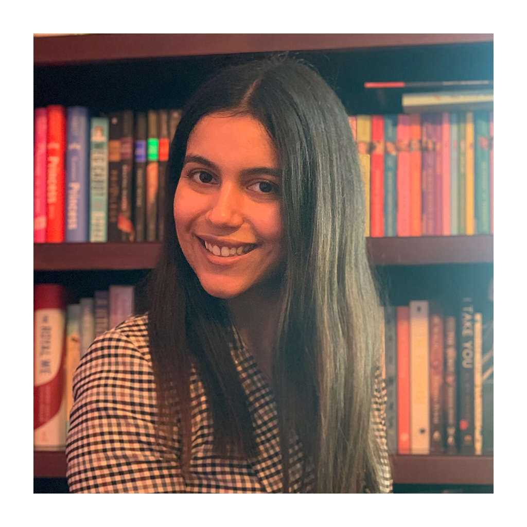 Female identifying person with long brown hair, smiling in front of bookshelf