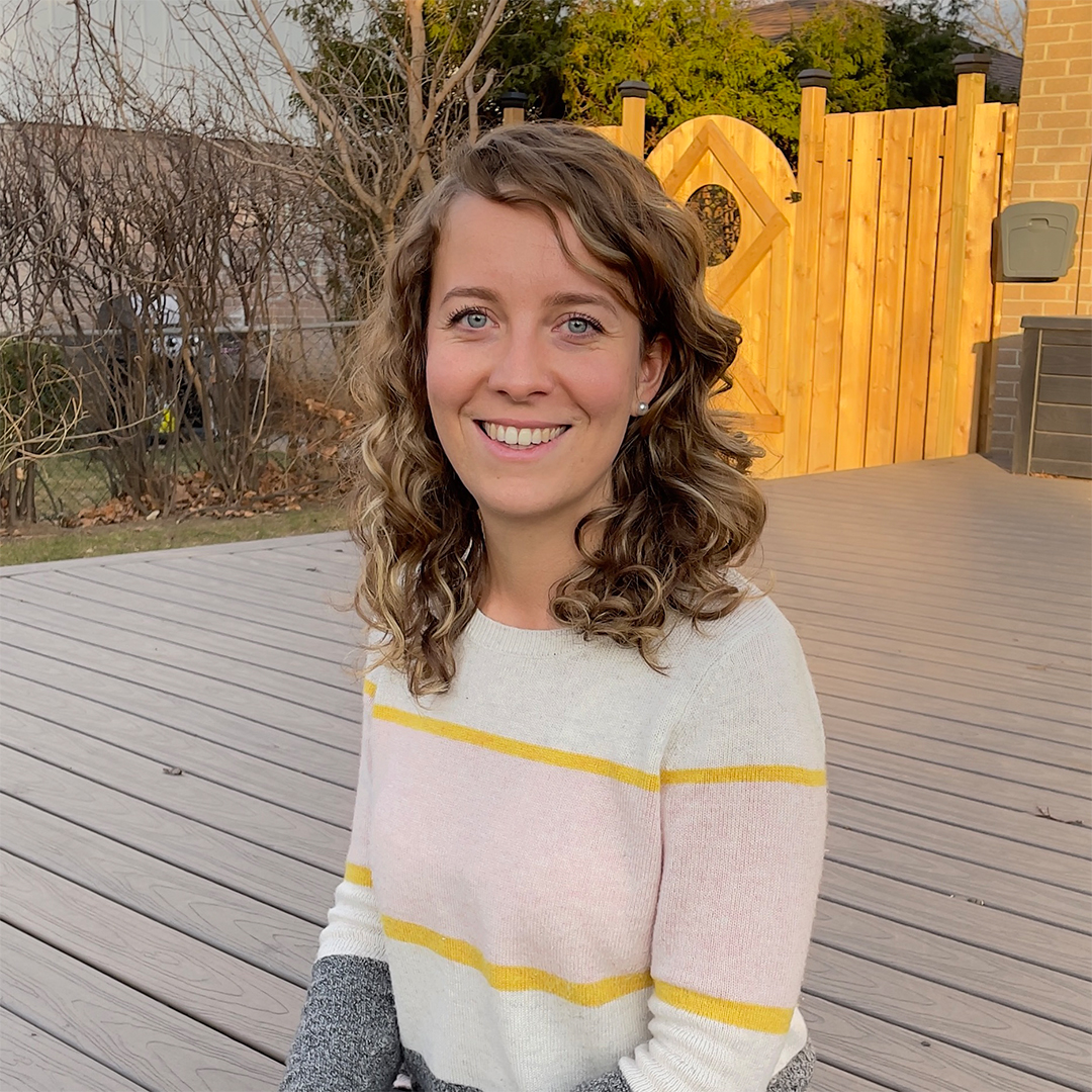 Female identifying person in striped sweater, smiling, outside on a deck