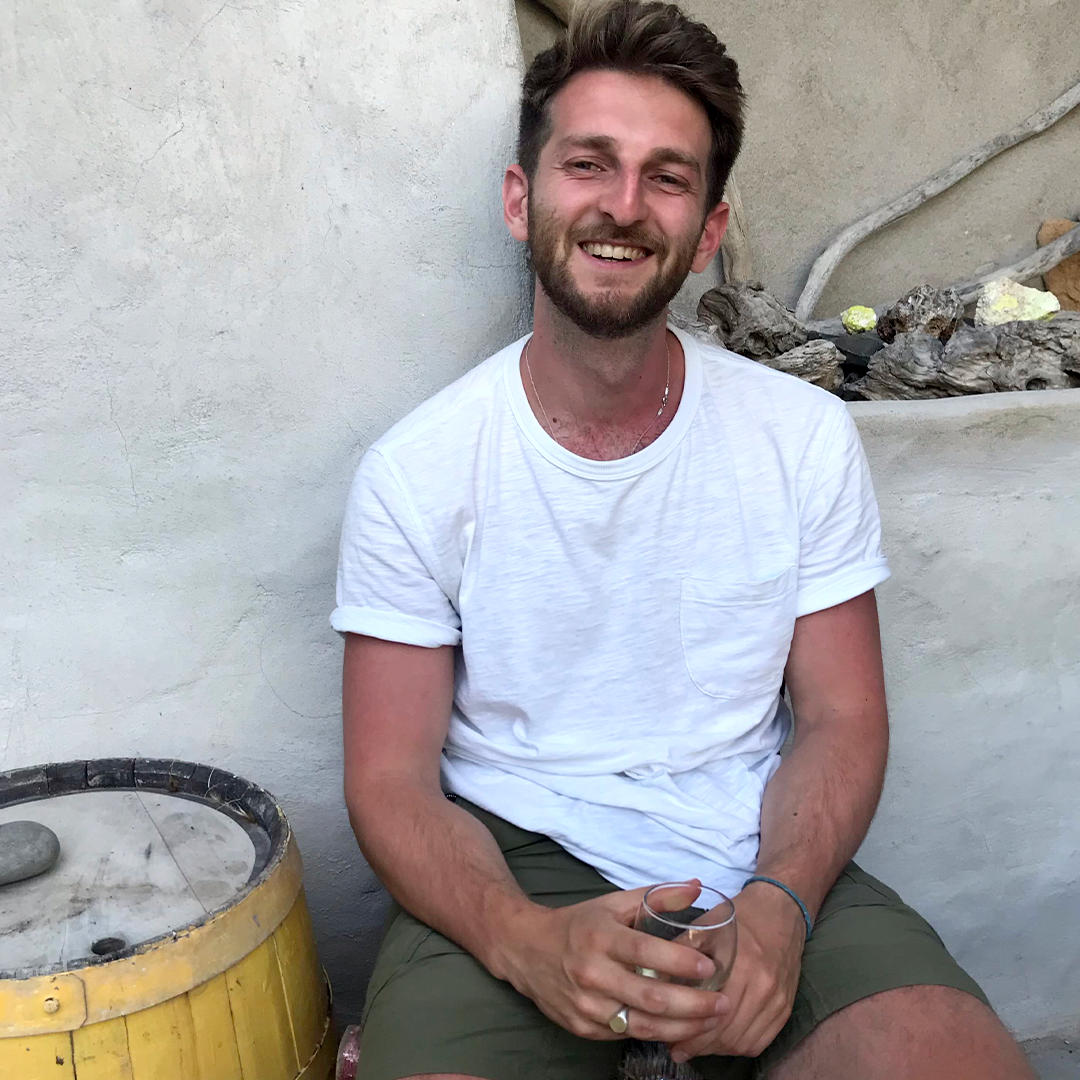 Male identifying person wearing a white t-shirt smiling, outside