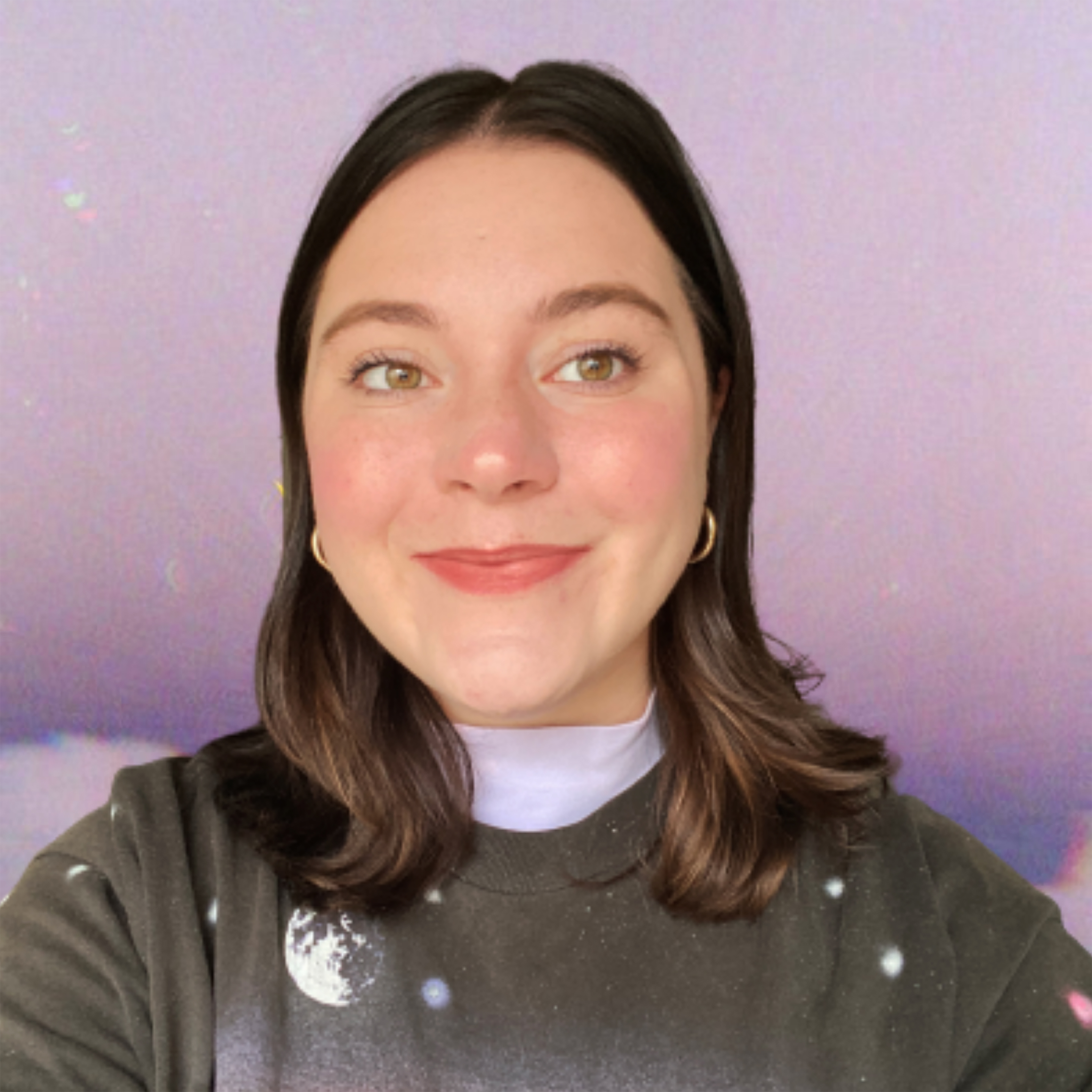 Female identifying person with brown hair and gold earings smiling, with purple sky background
