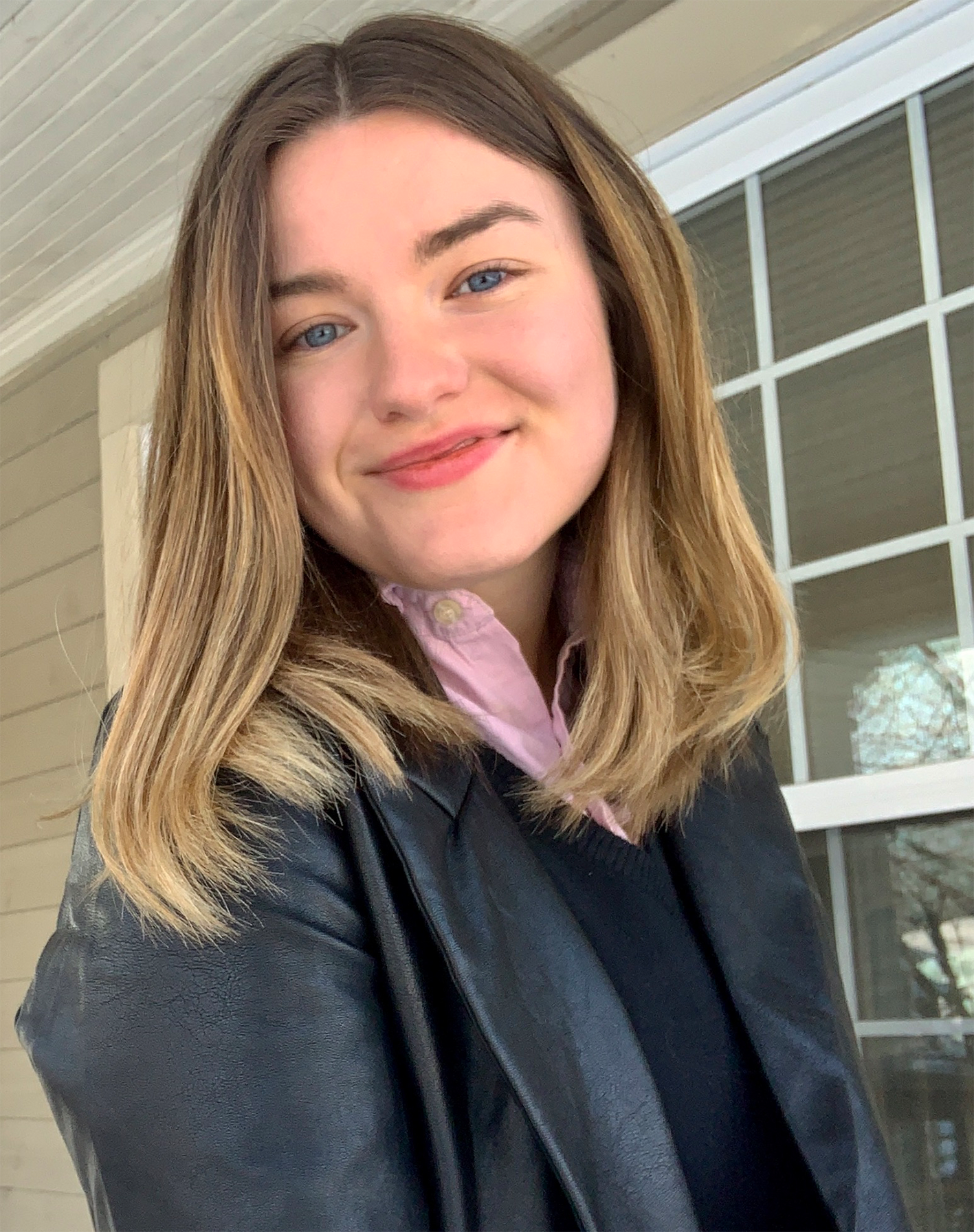 Female identifying person with blonde hair wearing a pink collar, smiling outside.
