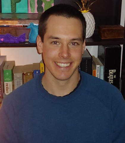 Male identifying person in blue shirt, in front of a bookshelf with a pineapple.