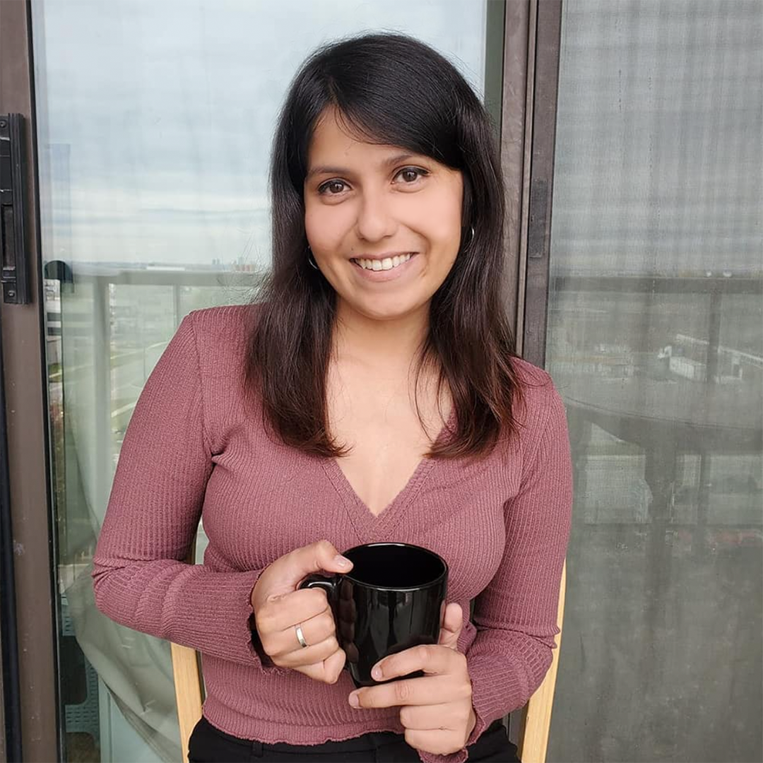 Female identifying person in pink top, smiling and holding a cup of tea