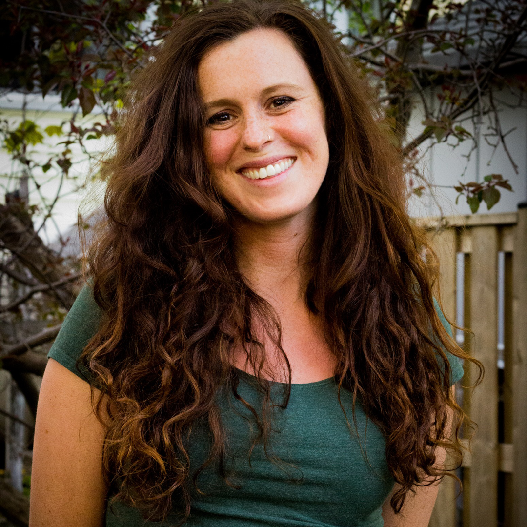 Female identifying person with long brown curly hair, smiling outside