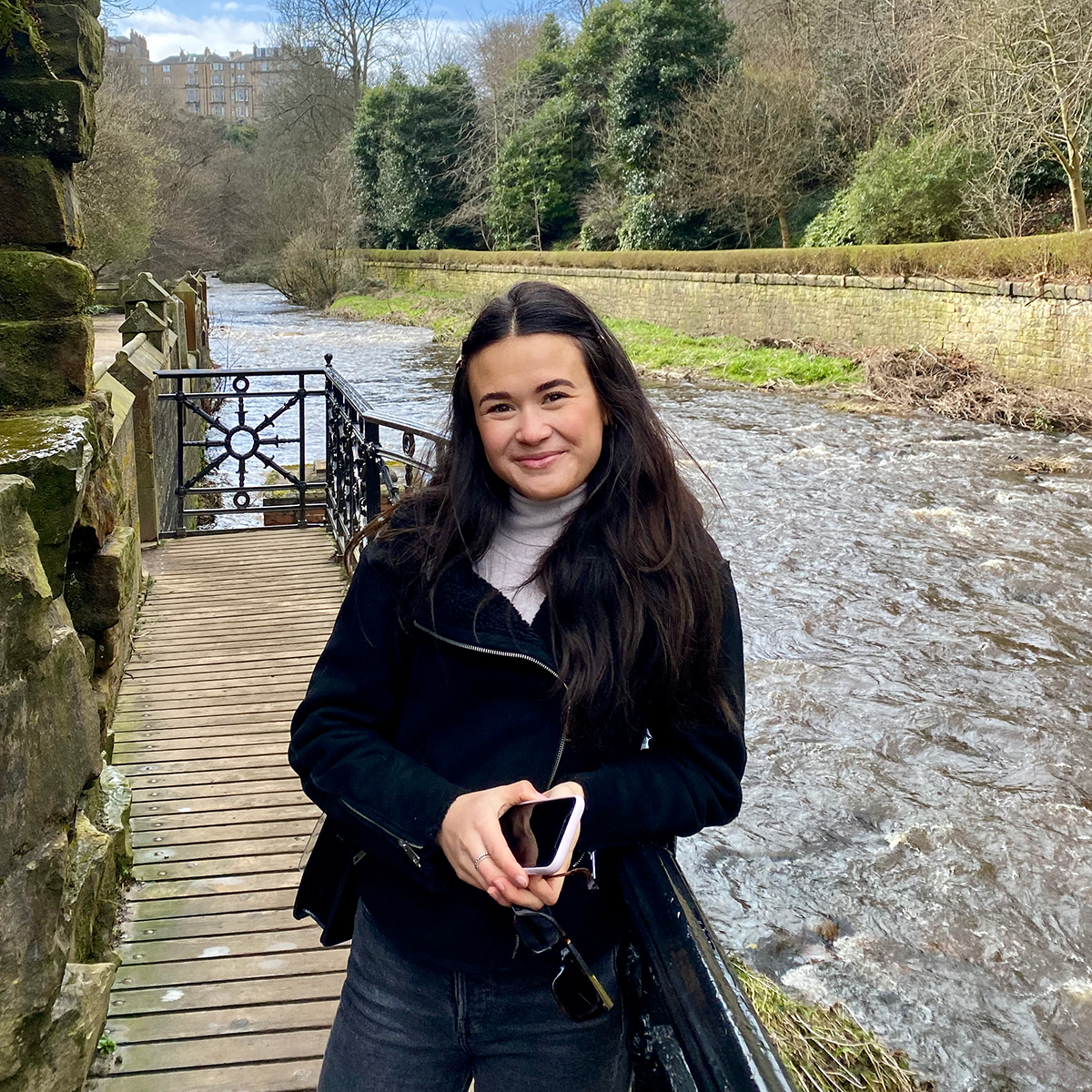 Female identifying person with brown hair, smiling beside river and trees