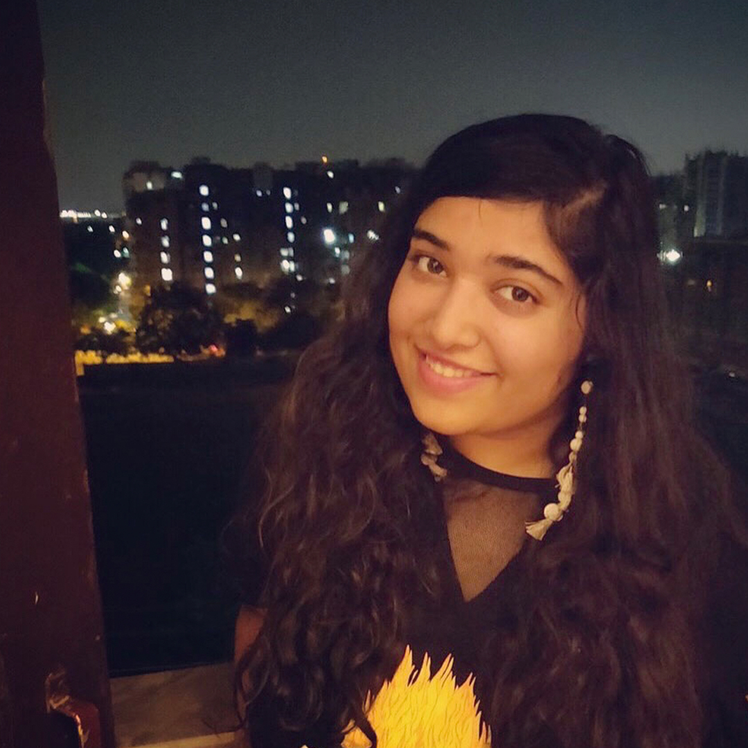 Female identifying person with long brown hair and long earings, against a night-time city background.